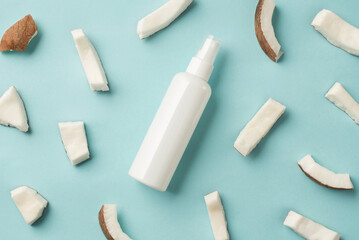 Top view photo of organic care product in white bottle with copyspace on isolated blue background with pieces of fresh coconut