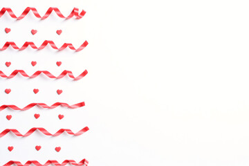 Red serpentine streamers and heart shaped confetti on white background, top view