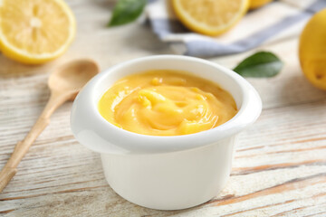 Delicious lemon curd in bowl on white wooden table, closeup