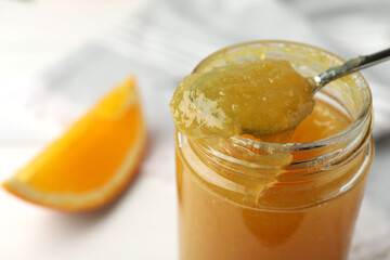 Spoon and jar with delicious orange marmalade on table, closeup. Space for text