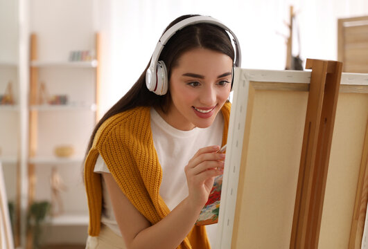 Beautiful young woman listening to music while drawing at home