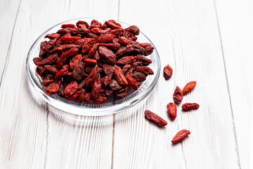  Dried goji berries in a glass plate on a white wooden table. Composition with organic, natural, Chinese wolfberries. Superfoods.
