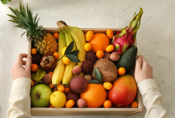 Woman with assortment of exotic fruits at table in kitchen, top view