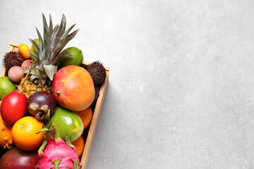 Crate with different exotic fruits on light grey table, top view. Space for text