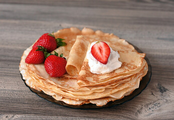 On a wooden table-pancakes with cottage cheese on a plate, decorated with strawberries, sliced and whole. Image with selective focus.