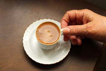 Hand holding cup of hot coffee on the table