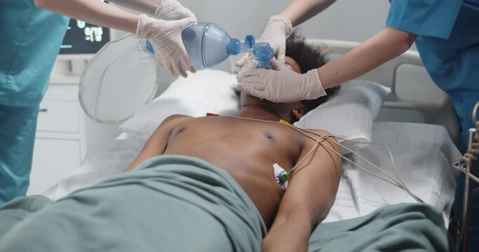 Nurse putting breathing bag on afro-american patient lying unconscious in hospital bed