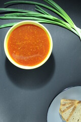 National Russian food red borscht soup in a yellow bowl plate next to lies onion green bread on a black background