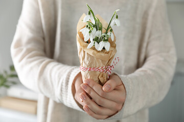 Woman holding paper bag with beautiful snowdrops and traditional cord martisor indoors, closeup. Symbol of first spring day - Powered by Adobe