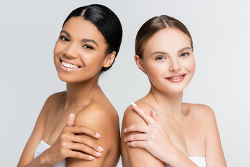 happy interracial women smiling while looking at camera isolated on grey