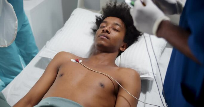 Doctors placing ecg electrodes on young unconscious afro-american patient