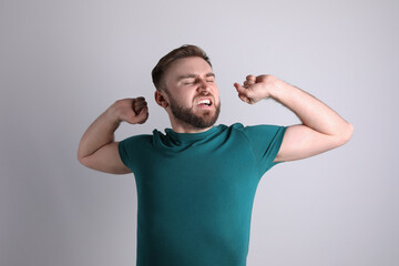 Sleepy young man yawning on light background
