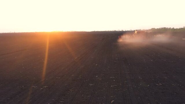 aerial view of tractor with the seeder working at the large field at the windy spring day
