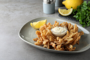 Fried blooming onion with dipping sauce served on grey table