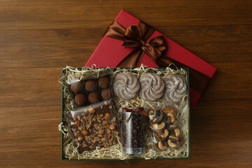 Gift box with chocolate and sweets on wooden table, top view
