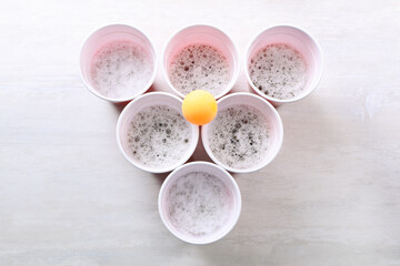 Plastic cups and ball for beer pong on white table, flat lay