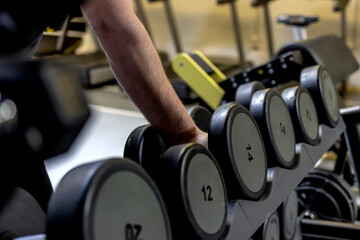 Fototapeta na wymiar Unrecognizable man taking dumbbells in a gym. Man holding dumbbell in gym. Rows of dumbbells in the gym with hand. Close up of dumbbell in fitness gym sport complex. Sport, healthy life and concept.