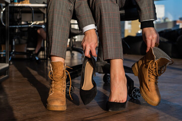 Business woman changes shoes with high heels on boots in the office. End of the working day. Tired...