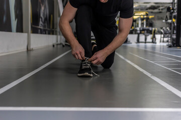 Fototapeta premium Unrecognizable man tying shoelace on sneakers, preparing for daily training. Shot of a unrecognizable man tying his shoelaces while exercising. Man crouching down and tying shoelaces before workout.