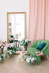 Fototapeta na wymiar Classical interior with mirror, sofa. White room with green sofa and two beautiful bouquets with roses, tulips and other flowers and greenery near