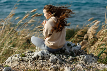 Young yoga woman meditation, mindfulness on seaside rock cliff edge. Beautiful sea view. Windy wheather