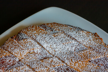 Close up of Neapolitan Pastiera, typical italian cake for Easter time. Filled with ricotta cheese, wheat and candied fruit, covered with powdered sugar. Shot on a black table and a white plate.