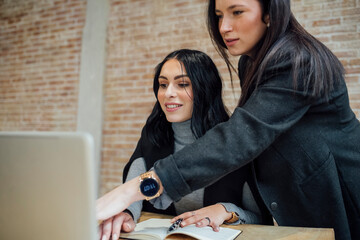 Two young mixed race women brainstorming, solving problem and planning business work indoor at...