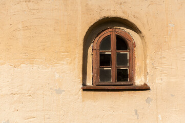 Fototapeta na wymiar Old building facade background with small arched window, yellow color stone texture