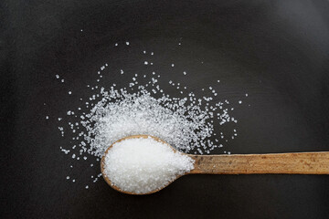 wooden spoon full of sugar crystals on a black plate,  top view