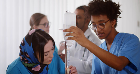 African male nurse teaching asian female intern making intravenous drip in hospital
