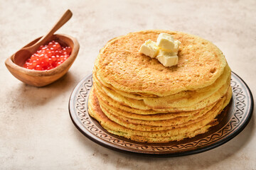 Crepes or thin pancakes stack with butter and red caviar on beautiful ceramic plate on an old brown concrete background. Top view, copy space. Homemade thin crepes for breakfast or dessert.