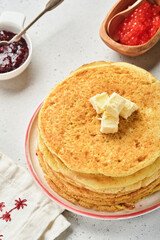 Crepes or thin pancakes stack with butter and raspberry jam on beautiful ceramic plate on an old gray concrete background. Top view, copy space. Homemade thin crepes for breakfast or dessert.