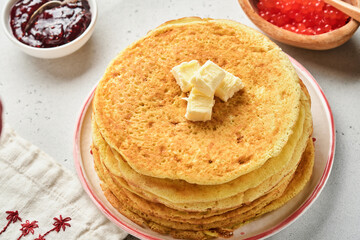 Crepes or thin pancakes stack with butter and raspberry jam on beautiful ceramic plate on an old gray concrete background. Top view, copy space. Homemade thin crepes for breakfast or dessert.
