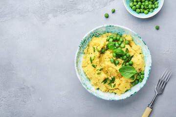 Mashed potato with butter, green peas, onions, basil in a white bowl on a light slate, stone or concrete background. Top view with close up.