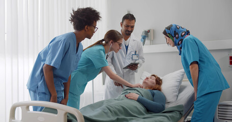 Diverse medical team examining young female patient lying in hospital bed - Powered by Adobe