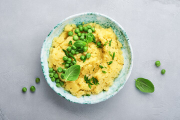 Mashed potato with butter, green peas, onions, basil in a white bowl on a light slate, stone or concrete background. Top view with close up.