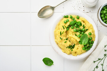Mashed potato with butter, green peas, onions, basil on white ceramic tile background. Top view with close up.