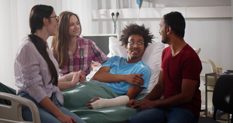 Diverse friends visit sick afro patient with broken arm in hospital.