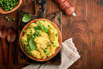 Mashed potato with butter, green peas, onions, basil on a rustic wooden background. Top view with close up.