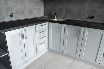 Modern minimalism style kitchen interior in monochrome tones. Custom kitchen with grey white facadesmdf and dark grey countertop with installed kitchen hood and sink. Modular kitchen from chipboard.