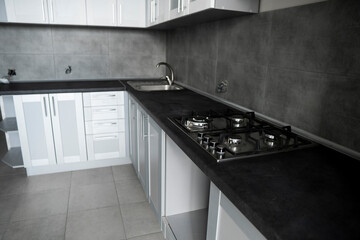 Modern minimalism style kitchen interior in monochrome tones. Custom kitchen with grey white facadesmdf and dark grey countertop with installed kitchen hood and sink. Modular kitchen from chipboard.