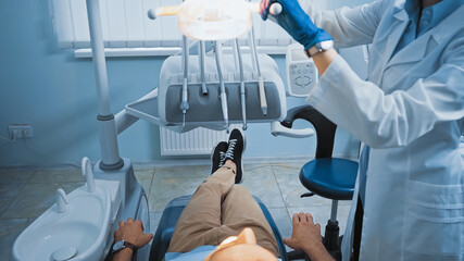 cropped view of dentist adjusting lamp above patient sitting in medical chair