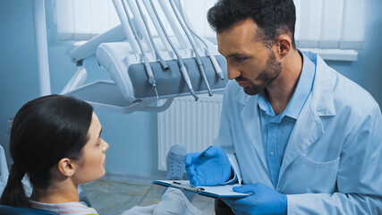 dentist holding clipboard while talking to patient near dental instruments