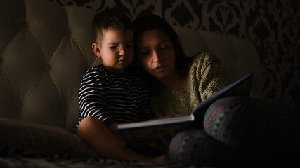 Mother with child read a book in the dark, before bedtime