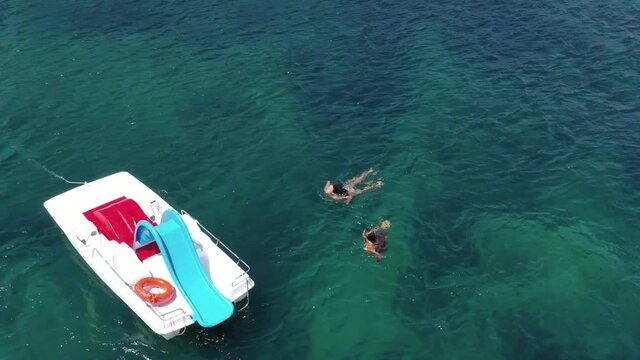 Happy girls bathe in the sea by sliding off the pedal boat
Aerial shot with drone on the calm and transparent sea.