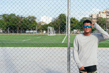 Urban young man wearing fashionable sunglasses near a fence. Attractive man enjoys the sun outdoors