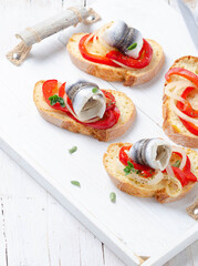 Summer sandwich with marinated anchovies and seasonal veggies on white wooden tray. Mediterranean diet.