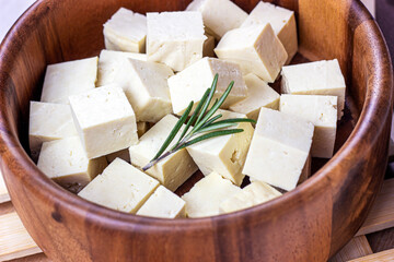 Raw organic vegetarian tofu cubes in round wooden bowl with fresh rosemary.