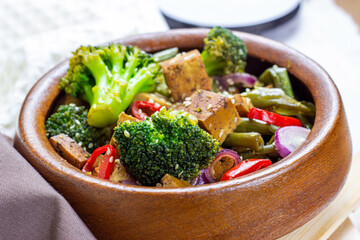 Homemade vegetarian fried tofu with vegetables (broccoli, pepper, onions and green beans) in the wooden bowl.