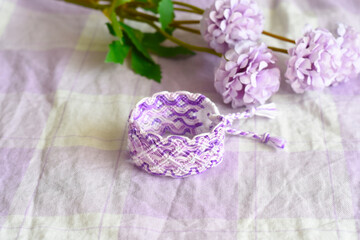 Purple DIY friendship bracelet with unusual braiding on lilac textile next to flowers